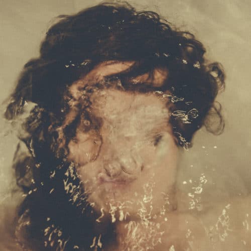 Woman's face underwater with bubbles from her breathing blurry and obscuring her face to represent anxiety