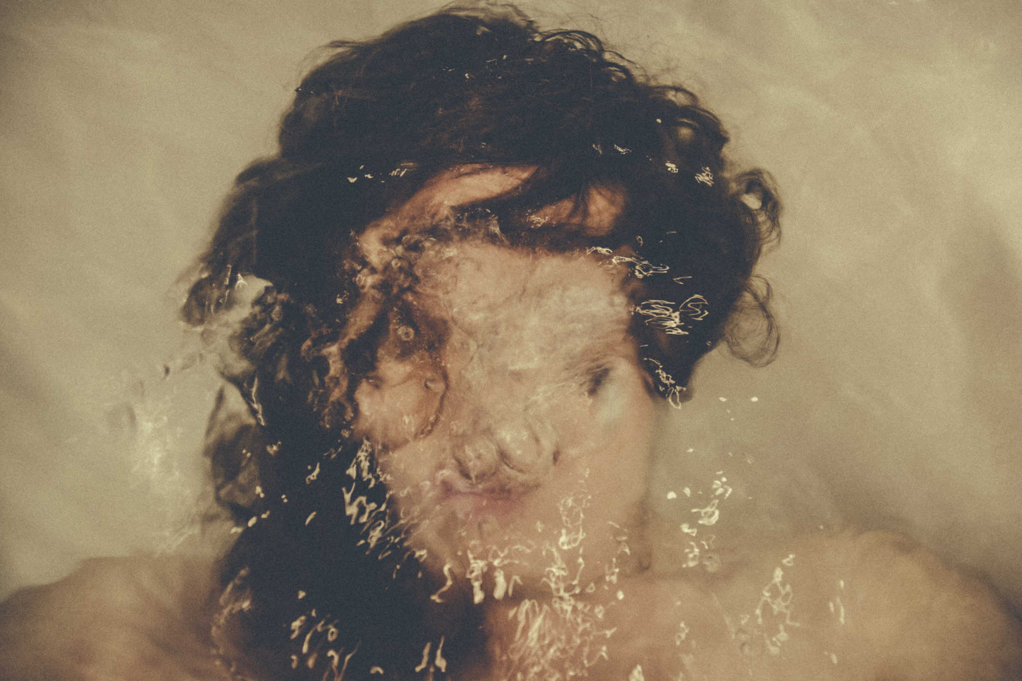 Woman's face underwater with bubbles from her breathing blurry and obscuring her face to represent anxiety