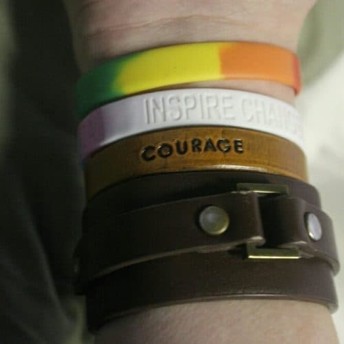 Wrist with multiple different types of wristbands on, one says Inspire and one says Courage