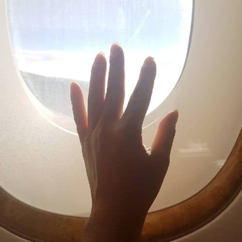 Hand placed on window of airplane with light shining though