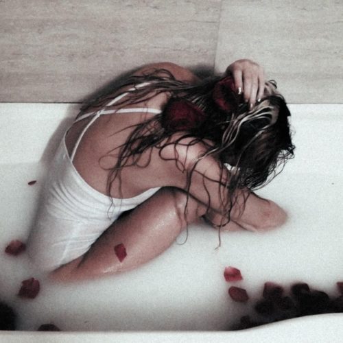 Woman sitting holding head in bathtub with milk and rose petals experiencing anxiety